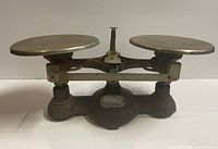 Front angled view of antique cast iron balance scale showing heavy base, dual round metal plates and central pointer.