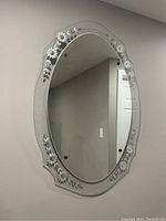 Oval Art Deco mirror mounted vertically on wall, showing etched floral design around edges.