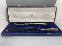 Open presentation box showing the two-piece carving set, with a knife and fork with wooden handles seated in molded blue velvet lining.