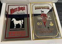 Two framed advertising mirrors side by side on white surface: White Horse Scotch Whisky on left and Beefeater London Distilled Dry Gin on right, highlighting colors and detail.