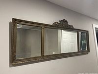 Full view of the large three-panel mirror mounted on a wall showcasing the overall design and gold gilt frame.