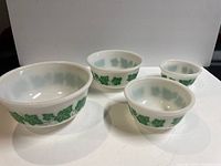 Four white milk glass nesting bowls with green ivy leaf design, arranged from largest to smallest.