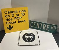 Lot showing all three signs together: yellow POP plastic sign, green Centre Rd metal street sign, and white metal safety eyewear sign.
