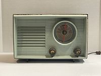 Front view showing light green front panel with speaker grille, two knobs, and circular dial gauge. The top and base edges show wear and some paint marks.