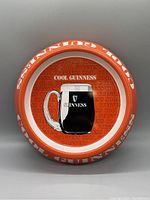 Front view of 1980s Guinness ashtray showing the full round design with orange background, central Guinness beer mug image and border text.