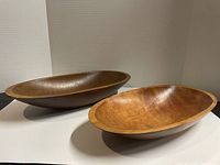 Pair of large oval wooden bowls placed on white background, different angles showing shape and relative size, worn condition visible