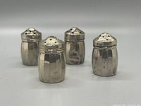 Four sterling silver salt and pepper shakers arranged on a flat surface.