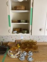 Amber glass bowls, leaf motif plates stacked inside cabinet, cups and saucers with leaf and graphic designs, miscellaneous dishes on kitchen counter
