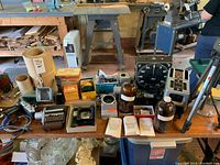 Wide shot showing multiple vintage photography items on table including cameras, flash units, glass bottles, cables, and boxes.