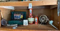 Photo showing Coleman two-burner camping stove, Utica Sportsman cutting tool with leather holster, Thermx Safety Heater, Primus camp fuel cans, Duracraft fan, and Primus portable stove on wooden shelf.