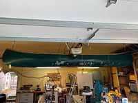 Canoe suspended from ceiling in a garage, visible chipping paint and wear on green surface.