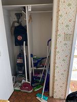 View of closet with Hoover Turbo Scrub Carpet Cleaner, Hoover floor polisher, Hoover cordless vacuum, and various Swiffer mop heads and cleaning supplies.