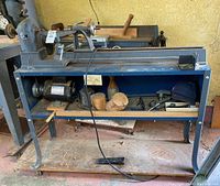 Full view of the electric metal lathe on blue metal stand with shelf and wheels in workshop environment.