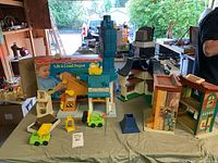 Wide shot of Fisher Price Lift & Load Depot playset with crane, toy vehicles, other vintage toys and boxes visible in background