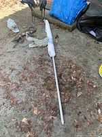 Patio umbrella, rolled up, white fabric, laid on the ground with two metal peacock statues in the background.