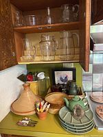 Glass and ceramic jugs and various kitchenware including a green teapot, tagine pot, and small dishes arranged on kitchen counter and shelves.