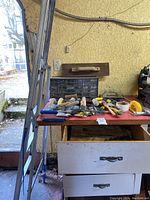 Photo of painting tools and hand tools on a red table surface, including paint rollers, scrapers, and a handsaw.