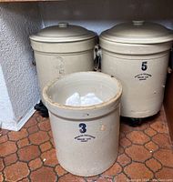 Three crocks grouped together on tile floor showing proportions and included lids
