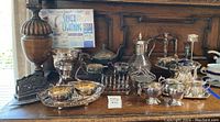 Wide view of all silver plated pieces arranged on wooden surface, includes a variety of dishes and sets.