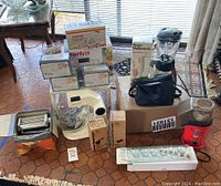 Wide shot of all items including Sunbeam Mixmaster, multiple Starfrit potato chip makers in boxes, Oster blender, air popper, pasta maker, Braun hand blender, coffee grinder, and other kitchen items.