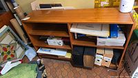 Front angled view of teak shelving unit filled with various office supplies and boxes.