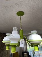 Front and side view of green ceiling light fixture with four white floral pattern glass shades and clear chimneys.