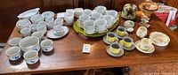 Wide shot of the table displaying multiple ceramic dishes, cups, mugs including Bunnykins set and other various ceramic pieces.