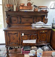 Front view of oak hutch sideboard with copper cookware and dishes on top shelf