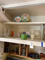 Photo of upper shelf holding vintage tins and assorted glass and ceramic vases including MCM orange glass vase