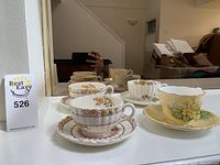 Four teacups with matching saucers displayed in front of mirror, including one yellow floral Aynsley set and three pastel floral Copeland sets.