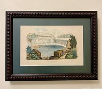 Front view of the framed waterfall art print showing the dark wooden frame and green mat border around the print.