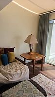 Full lamp on wooden side table with couch and pillows nearby, showing lamp shape and room setting.
