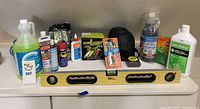 Photo showing all items included in the lot arranged in a row on white surface: spirit level, sprays, cleaning brushes, glue, and other liquids.