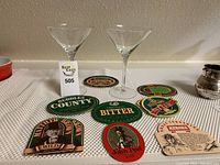 Two clear martini glasses with several English pub coasters arranged in front of them.