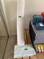 White memory foam bolster standing vertically next to a bed with folded towels and mattress on wooden slats.