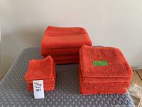 Photo showing full set of orange towels including bath towels, hand towels, and face cloths stacked neatly on a gray textured surface.