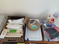 Overview of all items in the lot showing boxed interfacing sheets, woven basket, glues, spray adhesive, black fabric, and plastic storage boxes