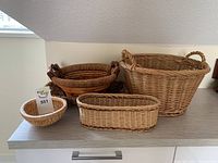 Front view of all five wicker baskets arranged on table showing different sizes and shapes.