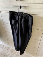Front view of black Club Monaco women's pants hanging on a wall, showing side pockets and slim tailoring.