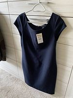 Black woman’s top hanging on a hanger with a tag attached, showing its cut and design.