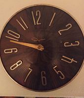Front view of the Ingraham mid-century wall clock showing the dark wood-toned plastic face with gold-colored numerals and hands, and brass-colored trim.