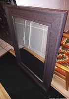 Side angle view of large rectangular mirror with dark plastic frame that looks like wood.