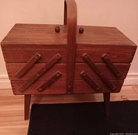 Closed Mid Century Modern accordion style sewing caddy box with wooden handle and angled legs.
