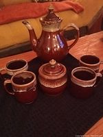 Photo showing entire tea set from an elevated angle, including teapot, sugar jar, and four mugs arranged on black cloth.