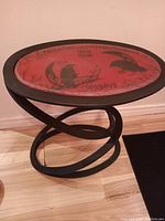 Photo of custom oval Ouija board table showing the red surface with black Ouija design, cast iron twisted base, and wood floor background.