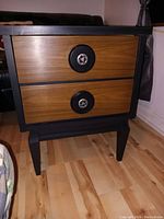Front view of vintage nightstand showing two wood drawer fronts with round black and metal decorative knobs and matte black painted frame and legs.