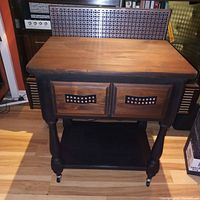Front view of vintage bar cart showing wood top, black painted legs, and two drawers with metal handles.