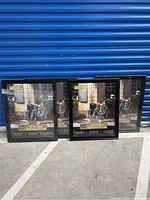 Four black poster frames standing side by side against a blue door. Three frames appear new, one may be used.