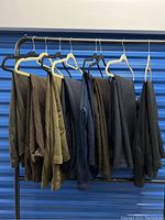 Eight pairs of men's dress pants hanging on hangers in various earth tones, blues, and blacks