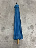 Closed blue wood umbrella on concrete surface showing handle and canopy.